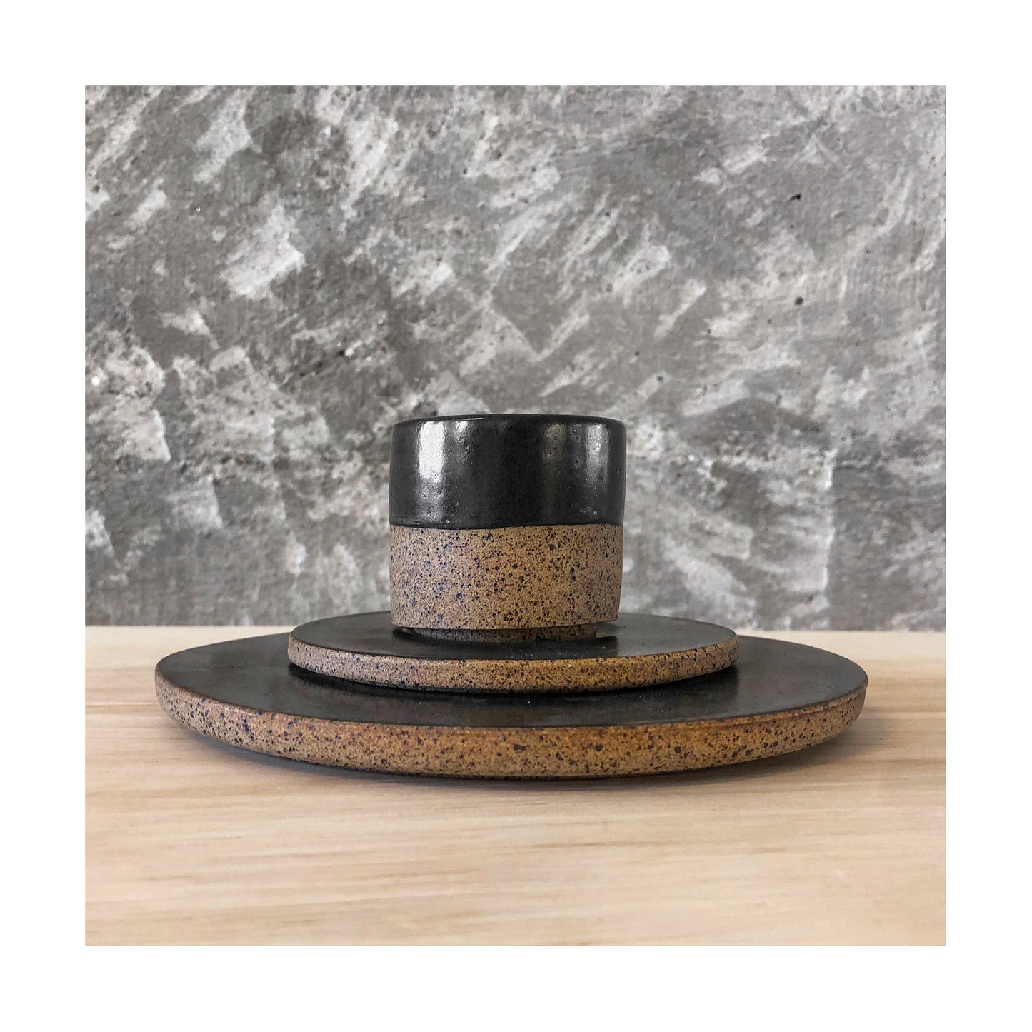 vista lateral de xícara de café e pires sobre prato de sobremesa em cerâmica artesanal com faixa de esmalte preto